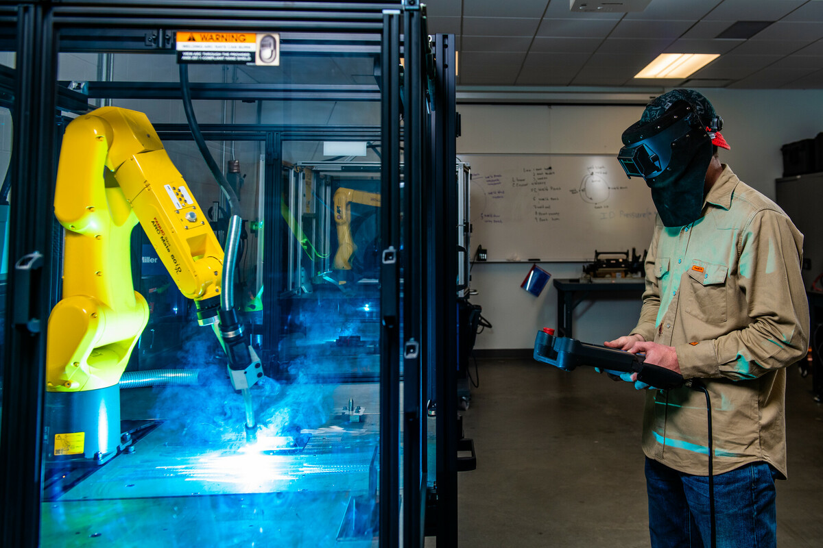 Student with welding helmet holding a operating a controller for the Fanic Arc Welder at the Technical Campus