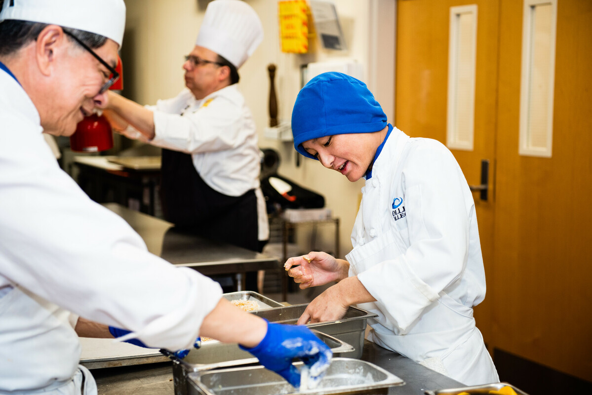 Culinary student preparing a dish alongside the class instructor.