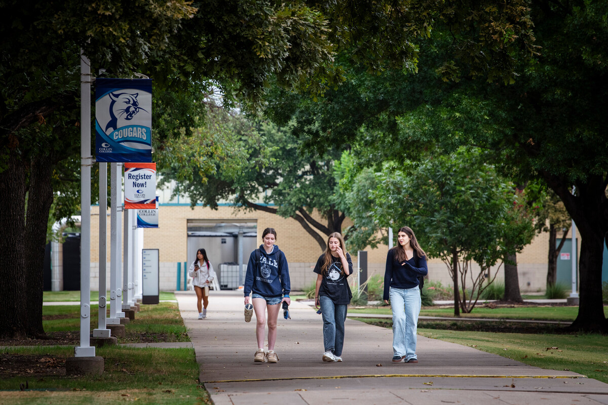 Students walking across campus. A registration sign hangs on a flagpole above them.