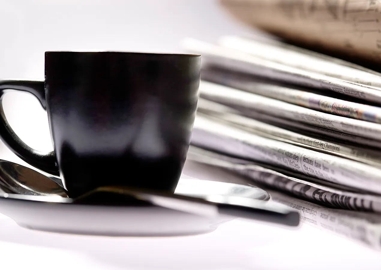 Black coffee cup in front of a stack of newspapers